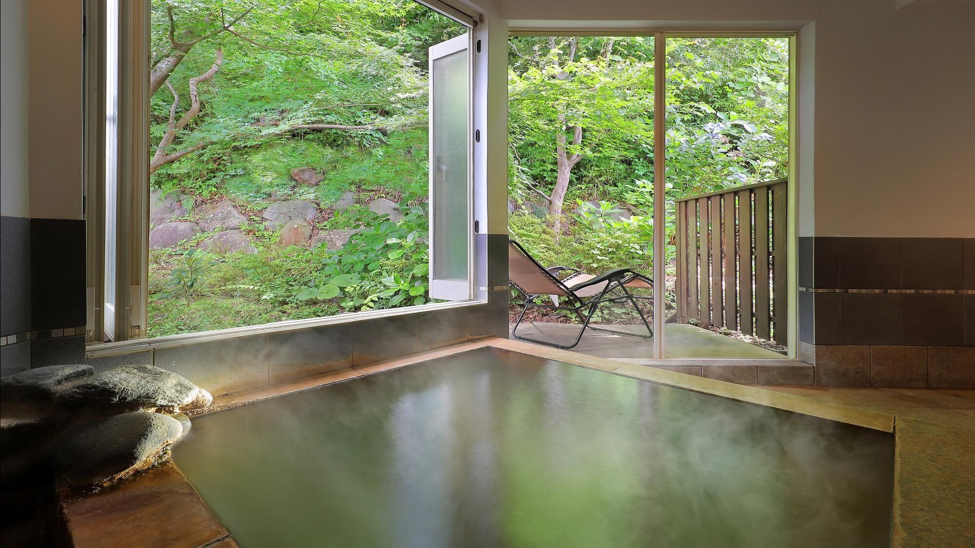 A spa area with a glass door leading to a garden, a stone bench, and a lounge chair.