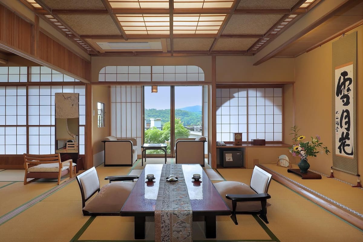A traditional Japanese-style room with tatami flooring, a low table with cushions, and sliding doors with a view of greenery.