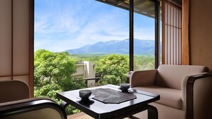 A balcony with a view of mountains, a table with a bowl and saucer, and a cushioned chair.