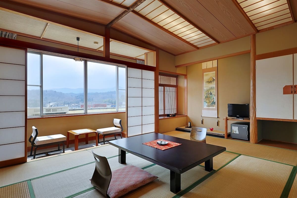 A traditional Japanese room with tatami flooring, a low table, a TV, and a view of the city.