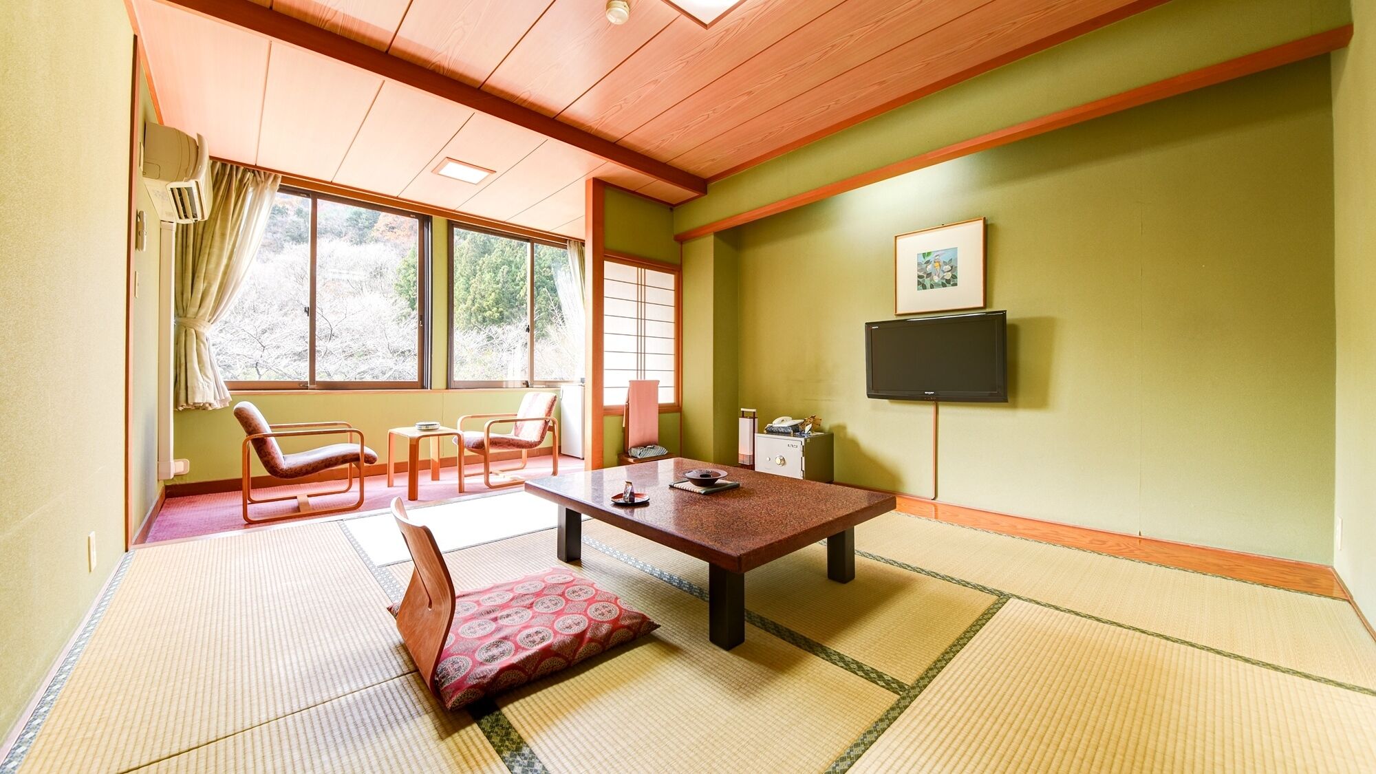 A room with tatami mats, a low table, chairs, a television, and a window with curtains.