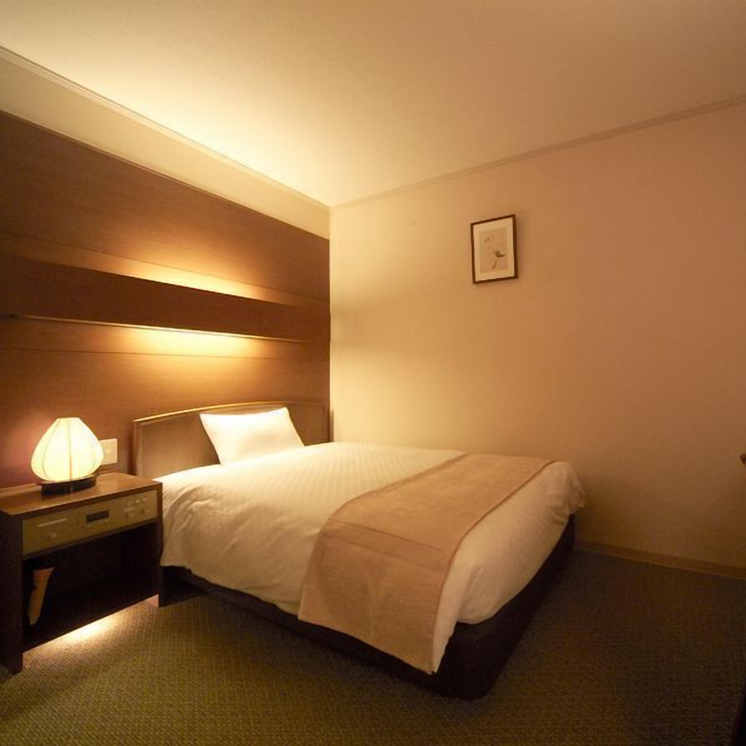 A hotel room with a bed, bedside lamp, and a framed picture on the wall.