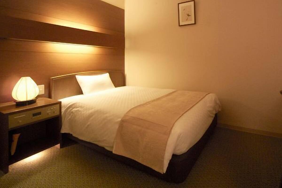 A hotel room with a bed, bedside lamp, and a framed picture on the wall.