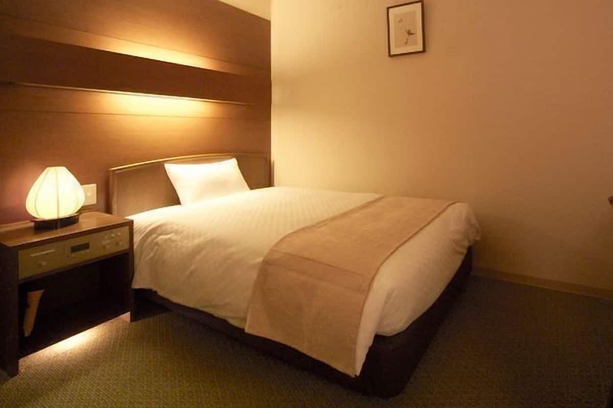 A hotel room with a bed, bedside lamp, and a framed picture on the wall.