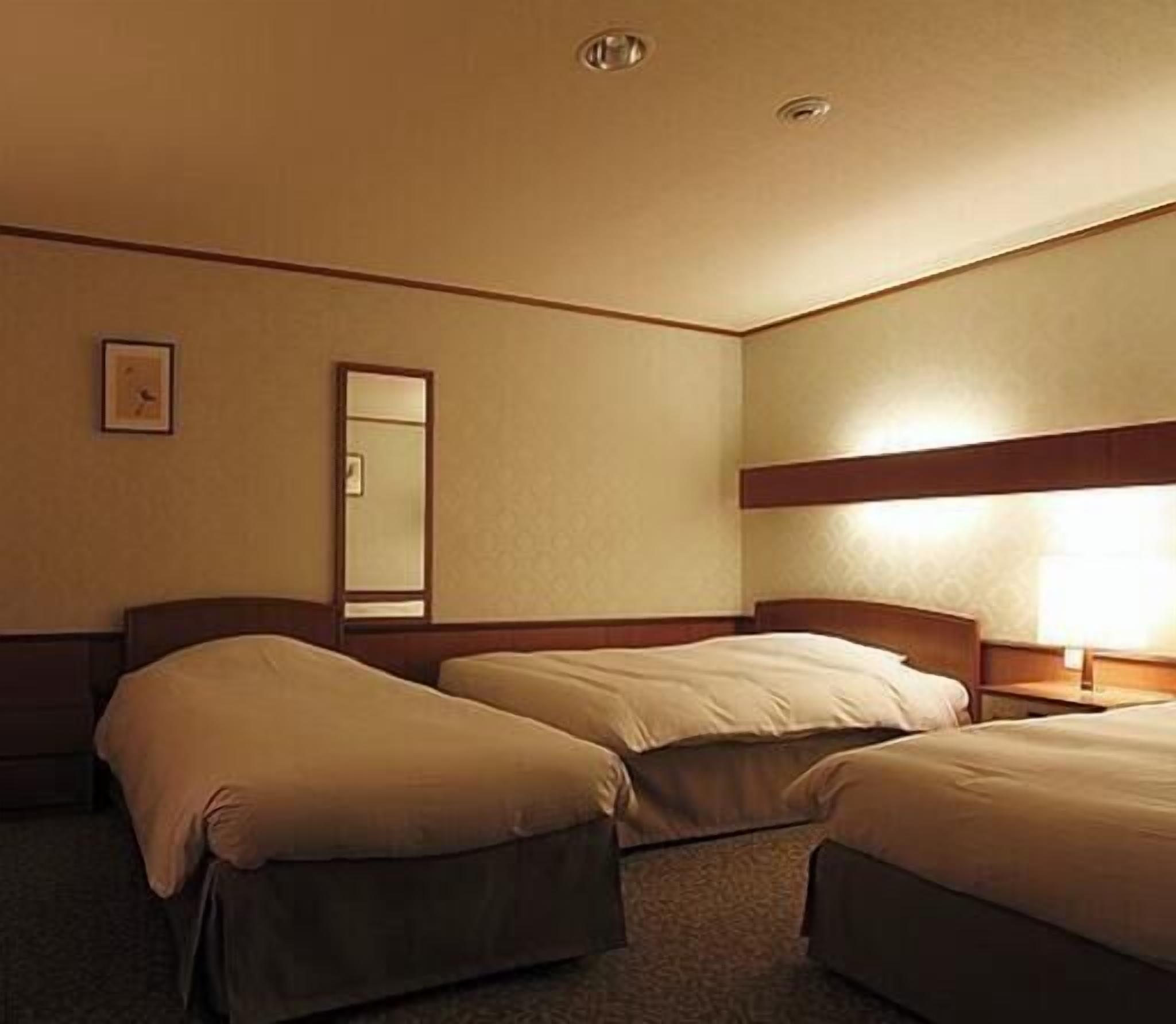 A hotel room with two beds, a bedside table, a lamp, a mirror, and a wall clock.