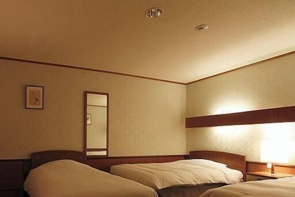 A hotel room with two beds, a bedside table, a lamp, a mirror, and a wall clock.