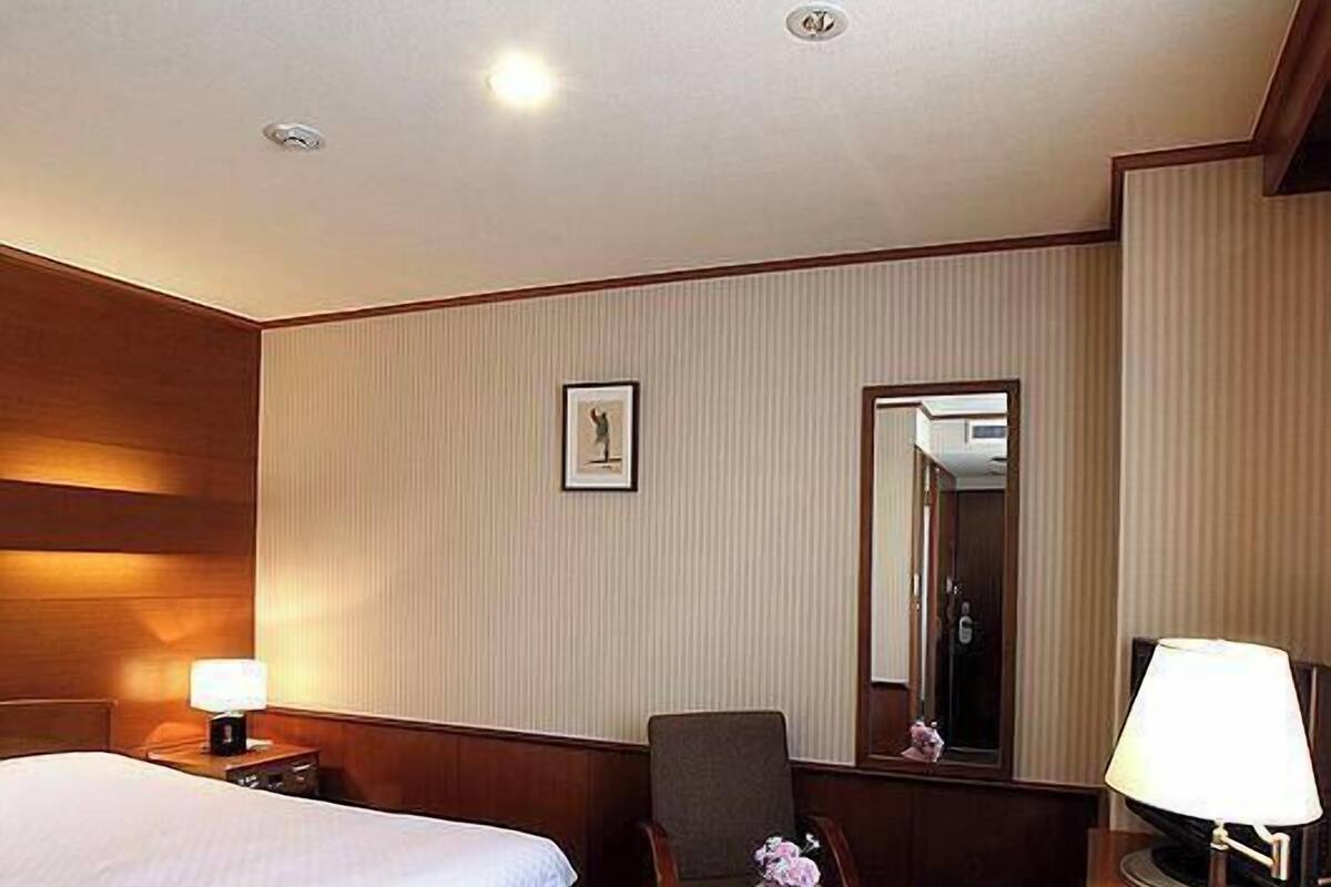 A hotel room with a bed, a chair, a small table, a lamp, a picture on the wall, and a mirror.
