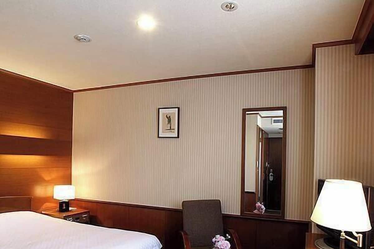 A hotel room with a bed, a chair, a small table, a lamp, a picture on the wall, and a mirror.