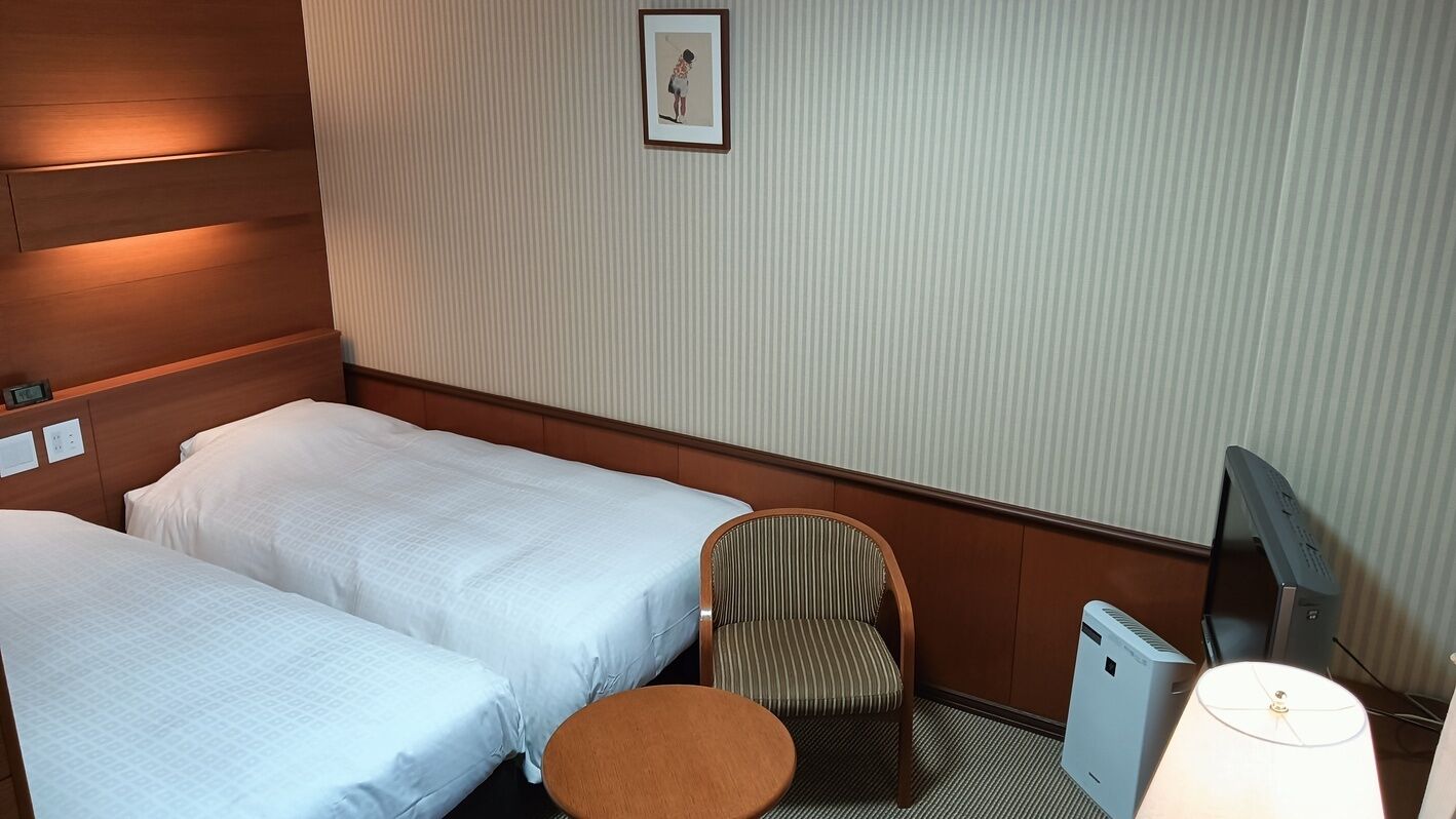 A hotel room with two beds, a chair, a small table, a TV, and a picture on the wall.