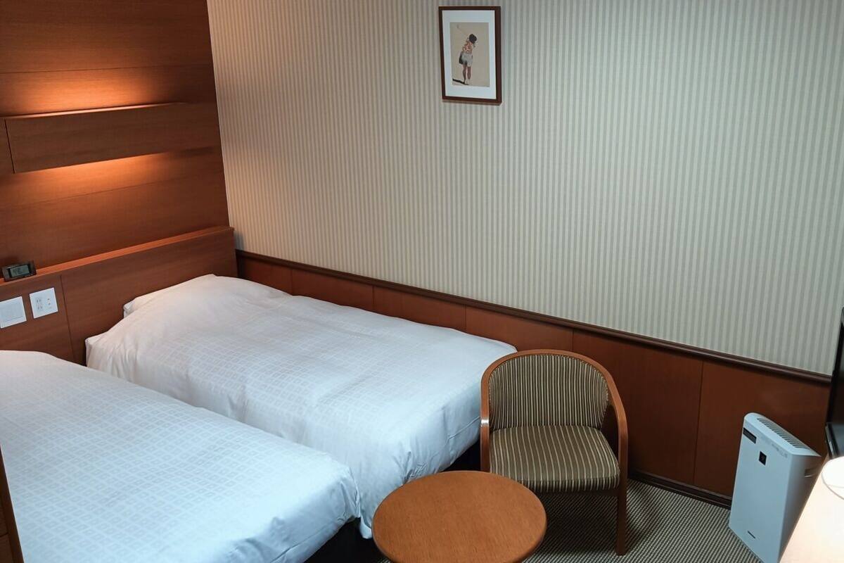 A hotel room with two beds, a chair, a small table, a TV, and a picture on the wall.