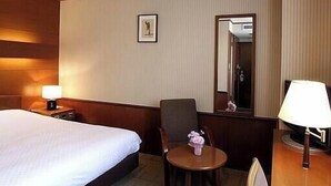 Et hotelværelse med en seng, en stol, et lille bord, en lampe, et billede på væggen og et spejl.
