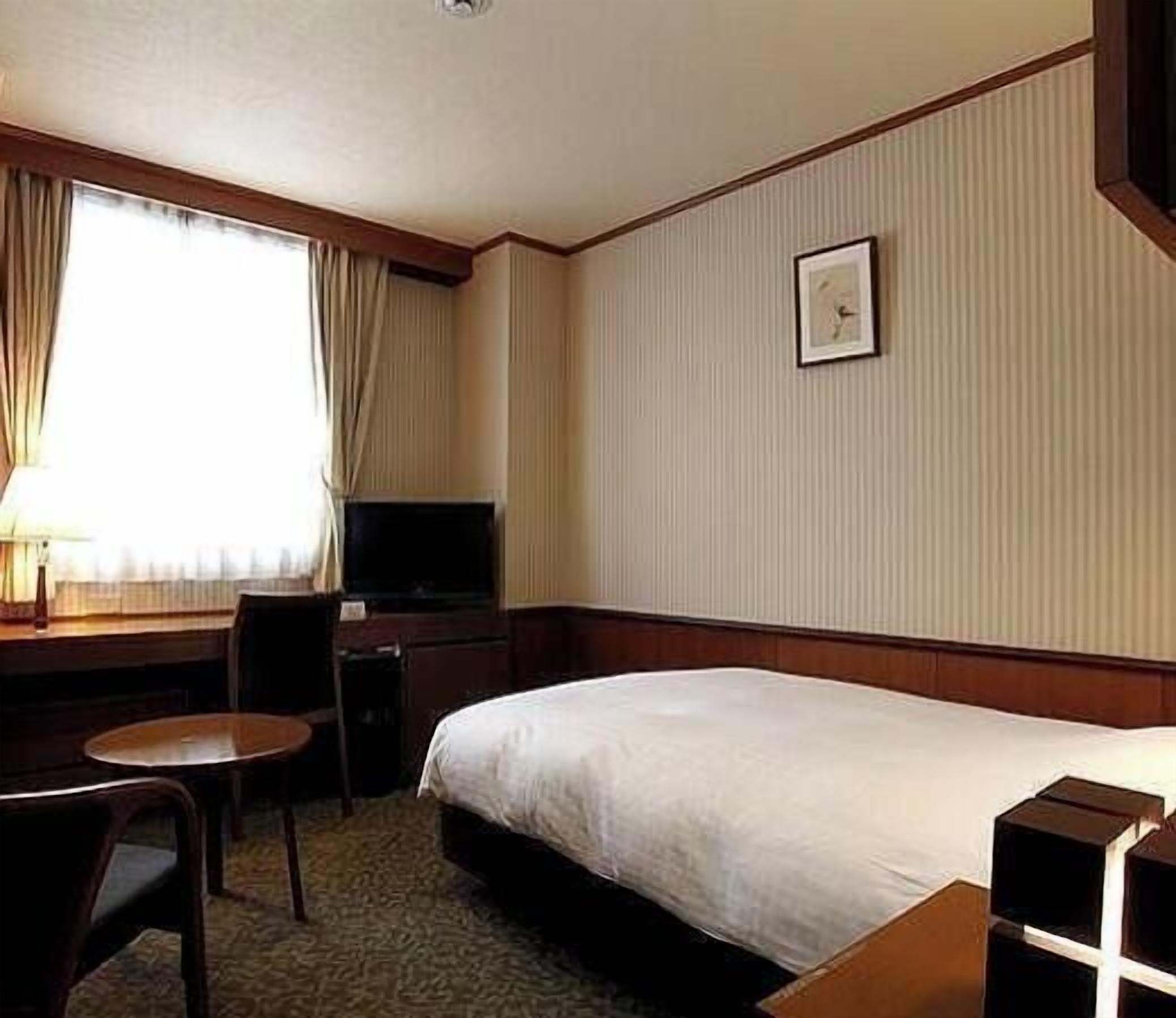 A hotel room with a bed, a desk, a chair, a television, and a window with curtains.