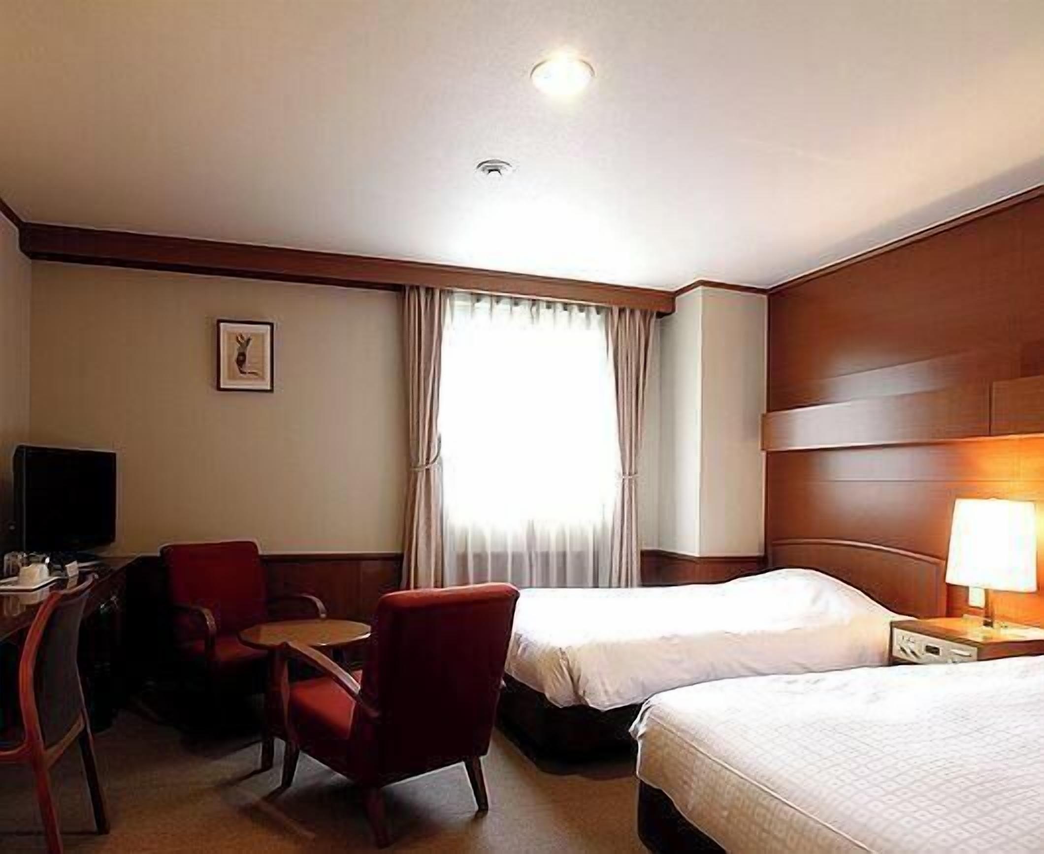 A hotel room with two beds, a desk with a chair, a television, and a window with curtains.
