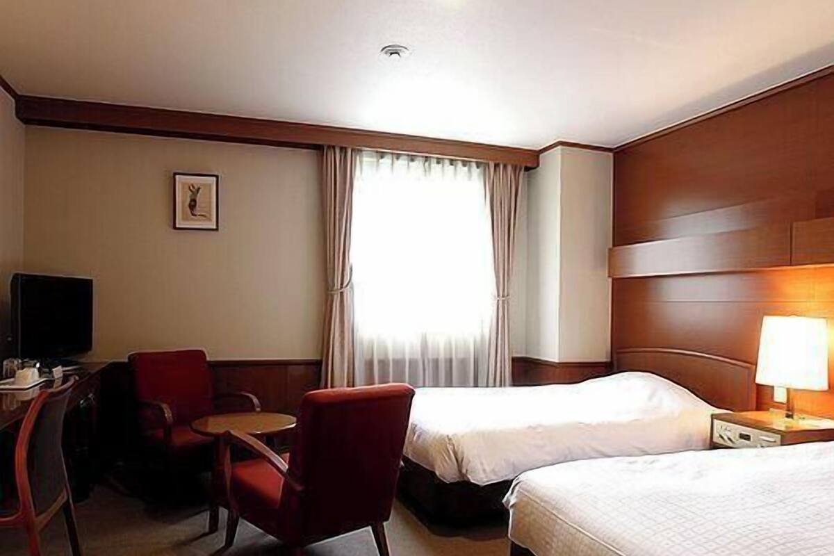 A hotel room with two beds, a desk with a chair, a television, and a window with curtains.