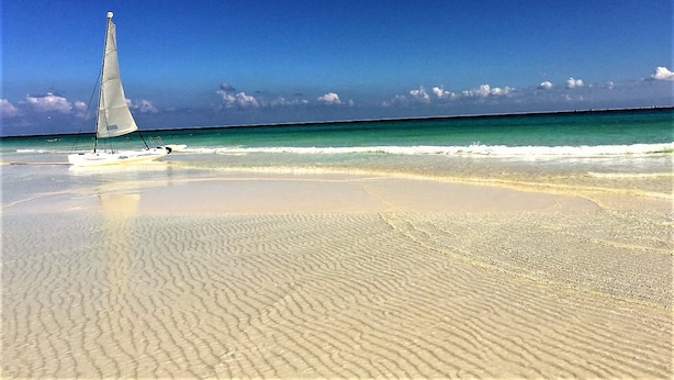 Una playa arenosa con un velero y aguas turquesas tranquilas.