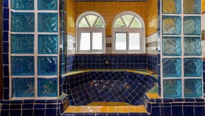 Un baño con pared de mosaicos, una bañera y dos ventanas.