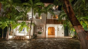Un edificio de dos pisos con un patio empedrado de piedra, rodeado de palmeras.
