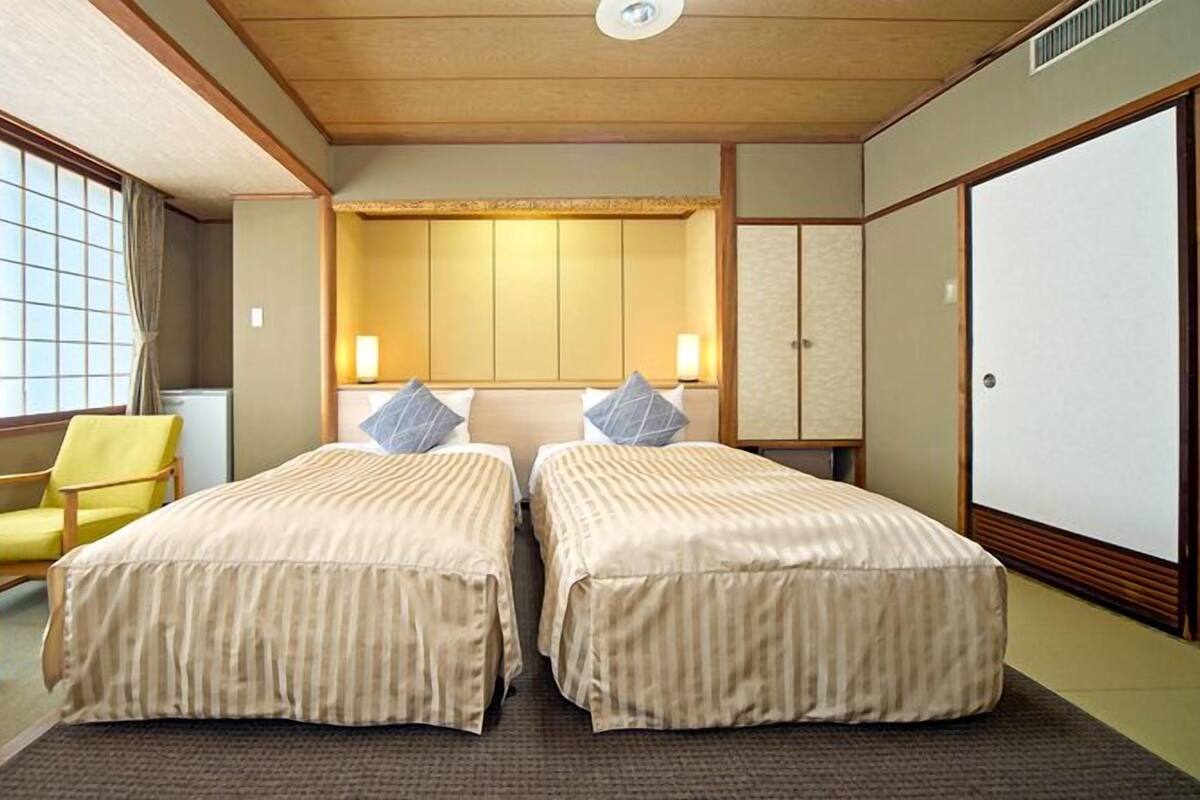 Ein Hotelzimmer mit zwei Betten, einem Sessel, einem Schreibtisch und einem Kleiderschrank.