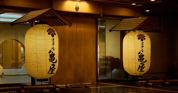 Dos faroles de papel iluminados con caracteres japoneses, vigas de madera y una decoración de interiores tradicional.