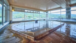 Un jacuzzi interior amplio con vistas a una cadena montañosa boscosa a través de ventanas grandes.