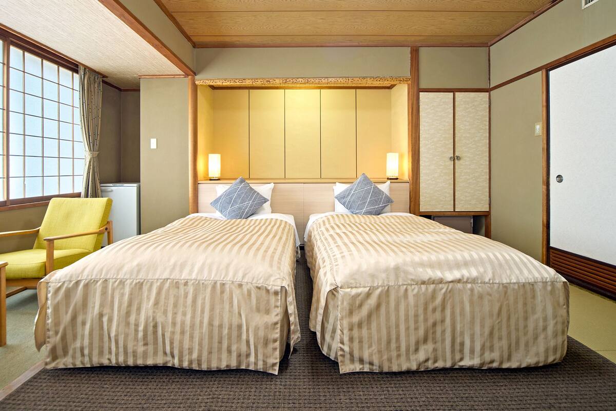 Ein traditioneller japanischer Raum mit zwei Betten, einem Holzstuhl und Schiebetüren.