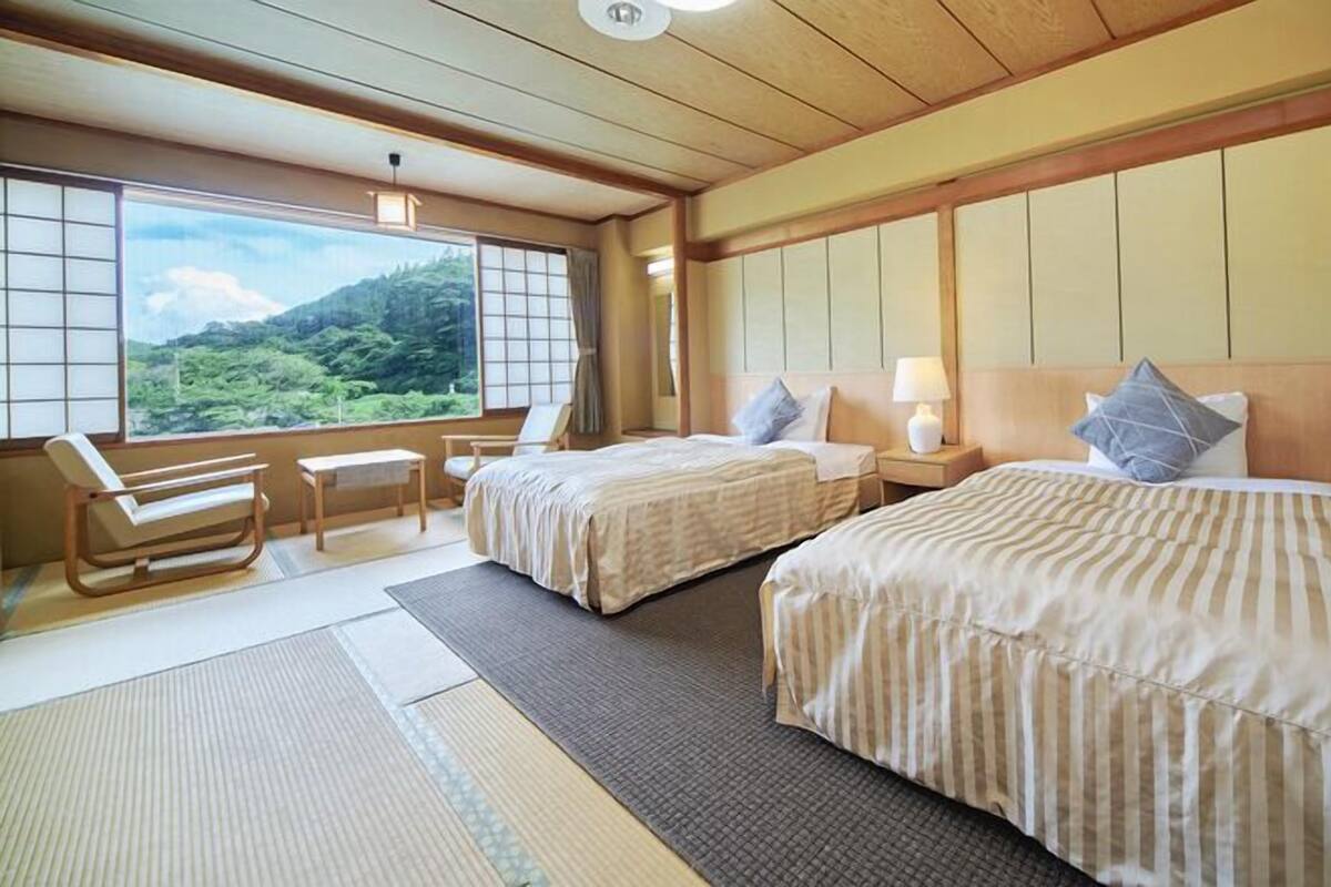Ein Hotelzimmer mit zwei Betten, einer Sitzecke mit Blick und traditionellem japanischen Tatami-Boden.