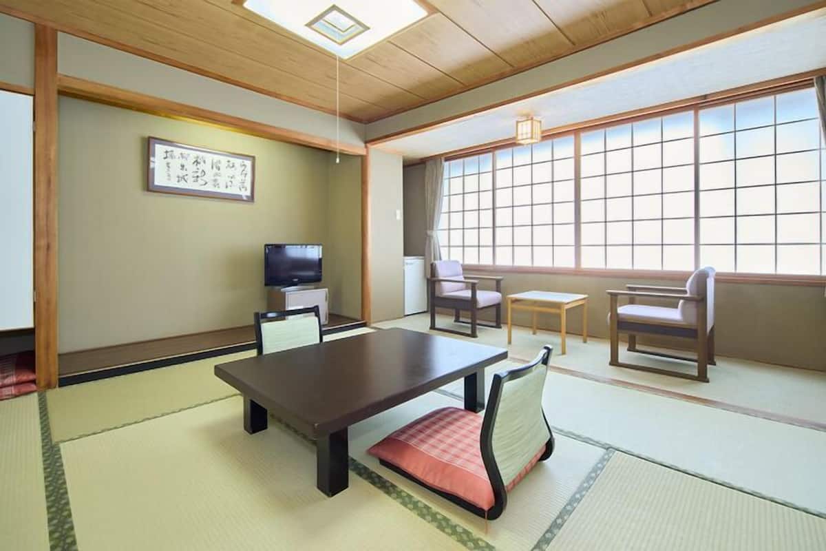 Ein traditioneller japanischer Raum mit Tatami-Böden, einem niedrigen Tisch, Stühlen, einem Fernseher und einem großen Fenster.