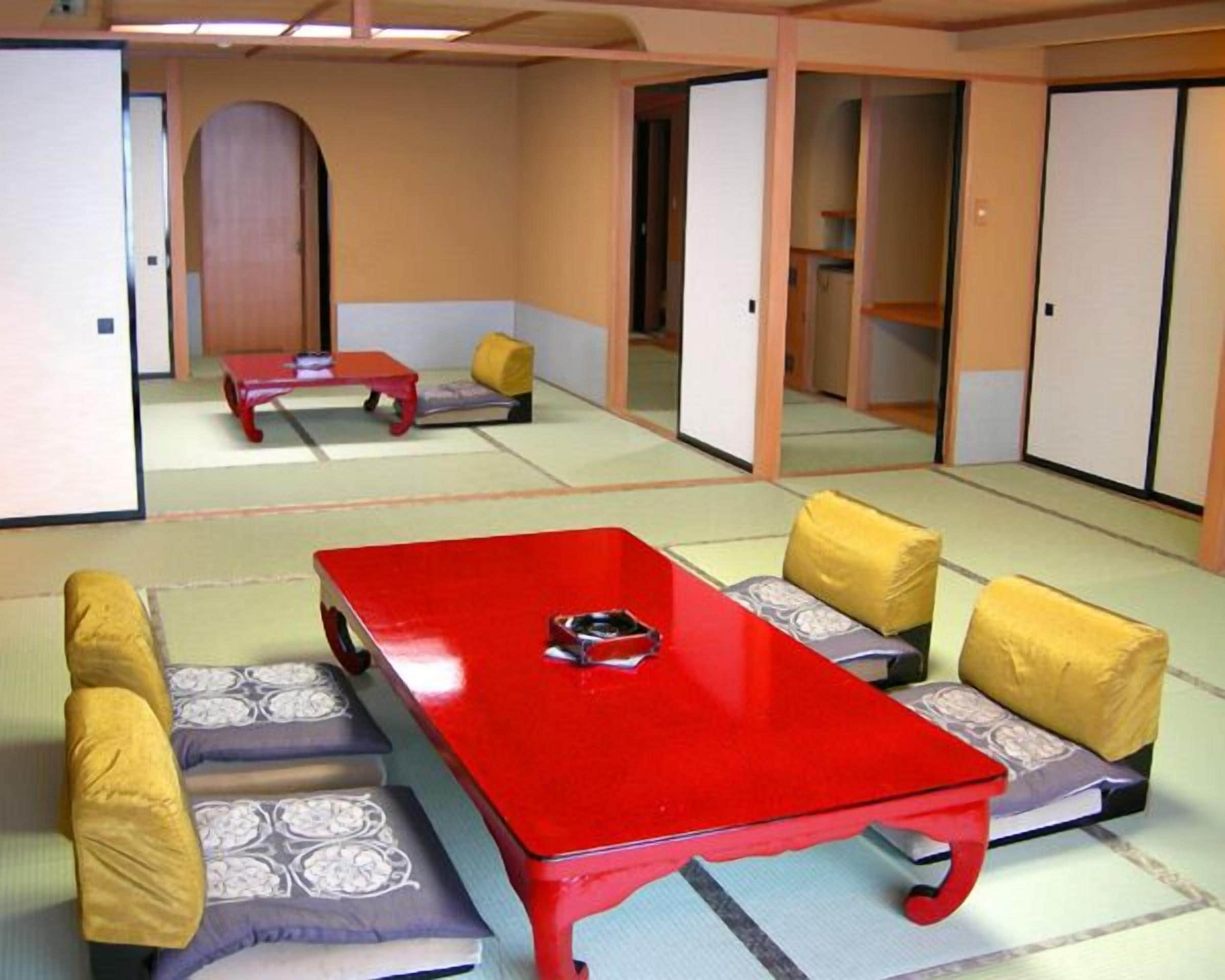 Habitació tradicional amb tatami, taula vermella, coixins baixos i portes corredisses.
