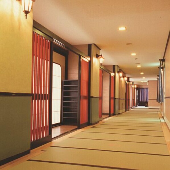 Un couloir doté de portes coulissantes traditionnelles, d’un plancher en bois et de luminaires fixés au mur.