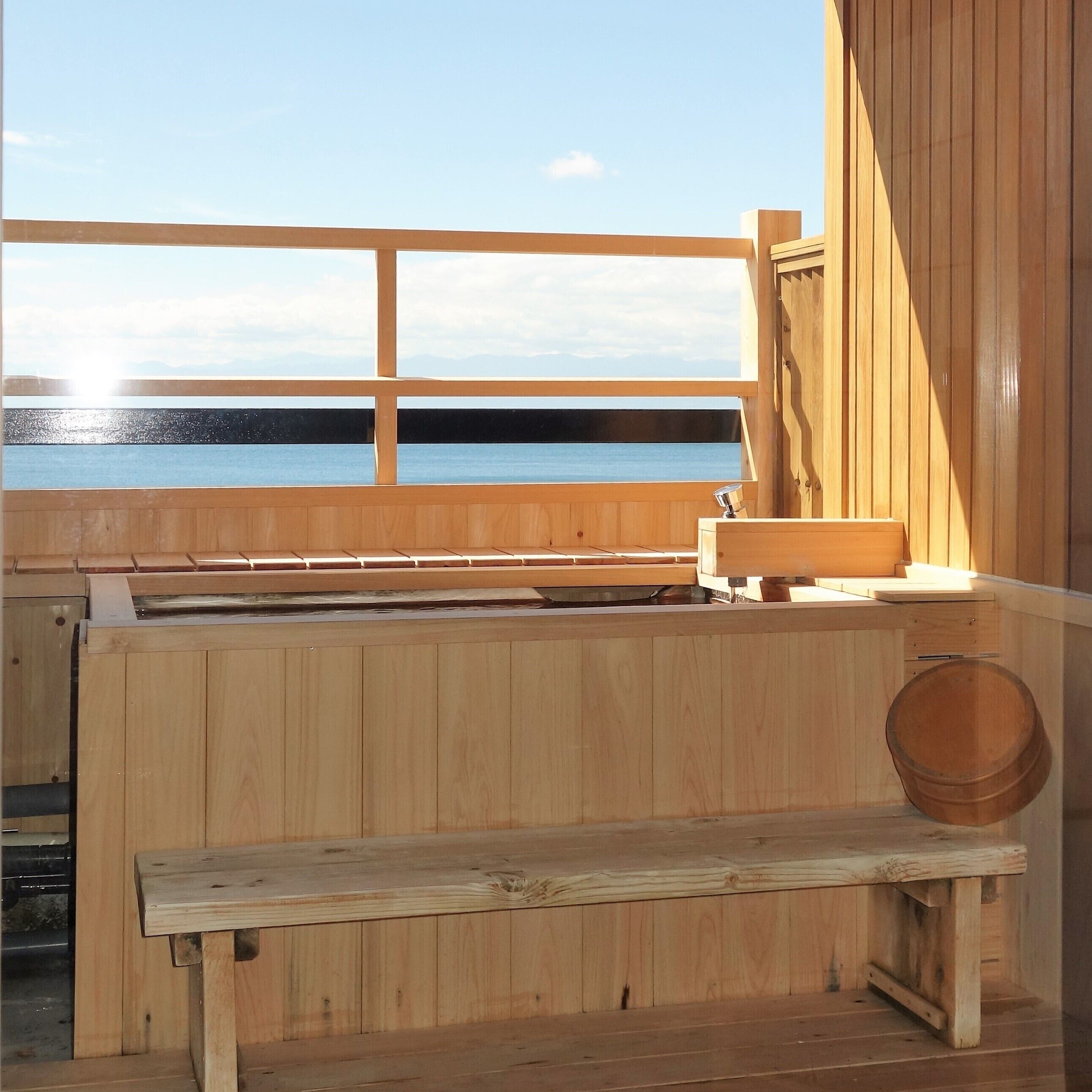 Una sauna de madera con un banco, un lavabo y vistas al agua.