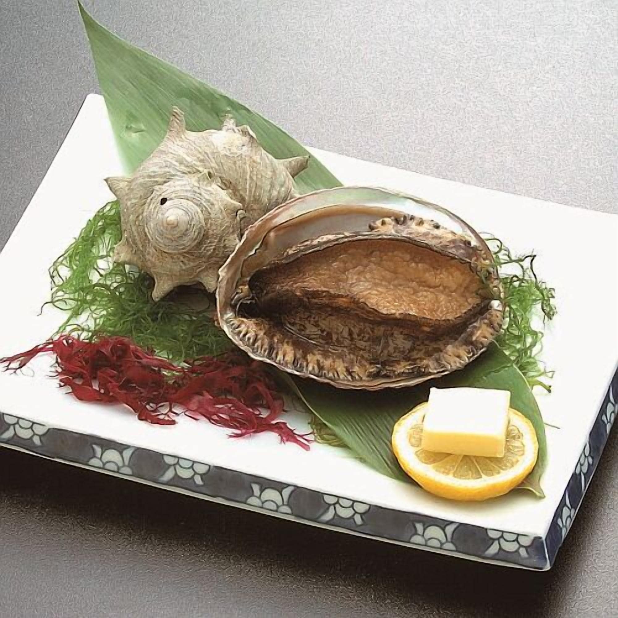 A plate with a shell, greens, and a lemon wedge.