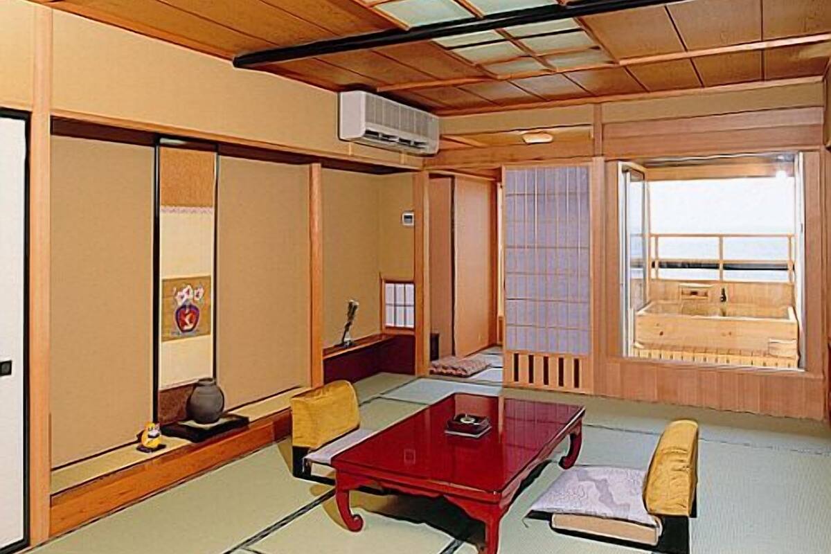 A traditional Japanese room with tatami flooring, a low wooden table, and a view of the sea through a sliding door.
