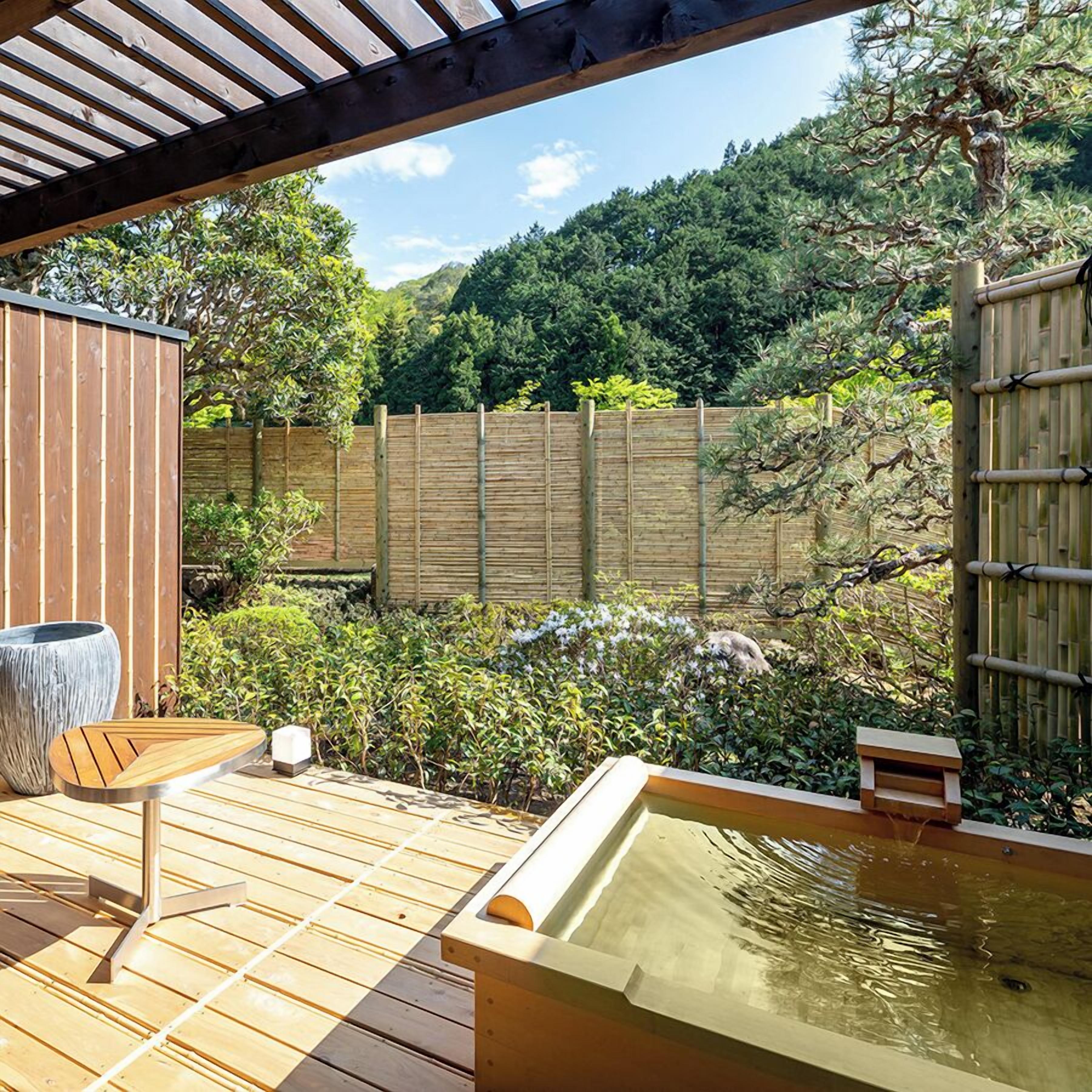 A wooden deck with a hot tub, a seating area, and a bamboo fence.
