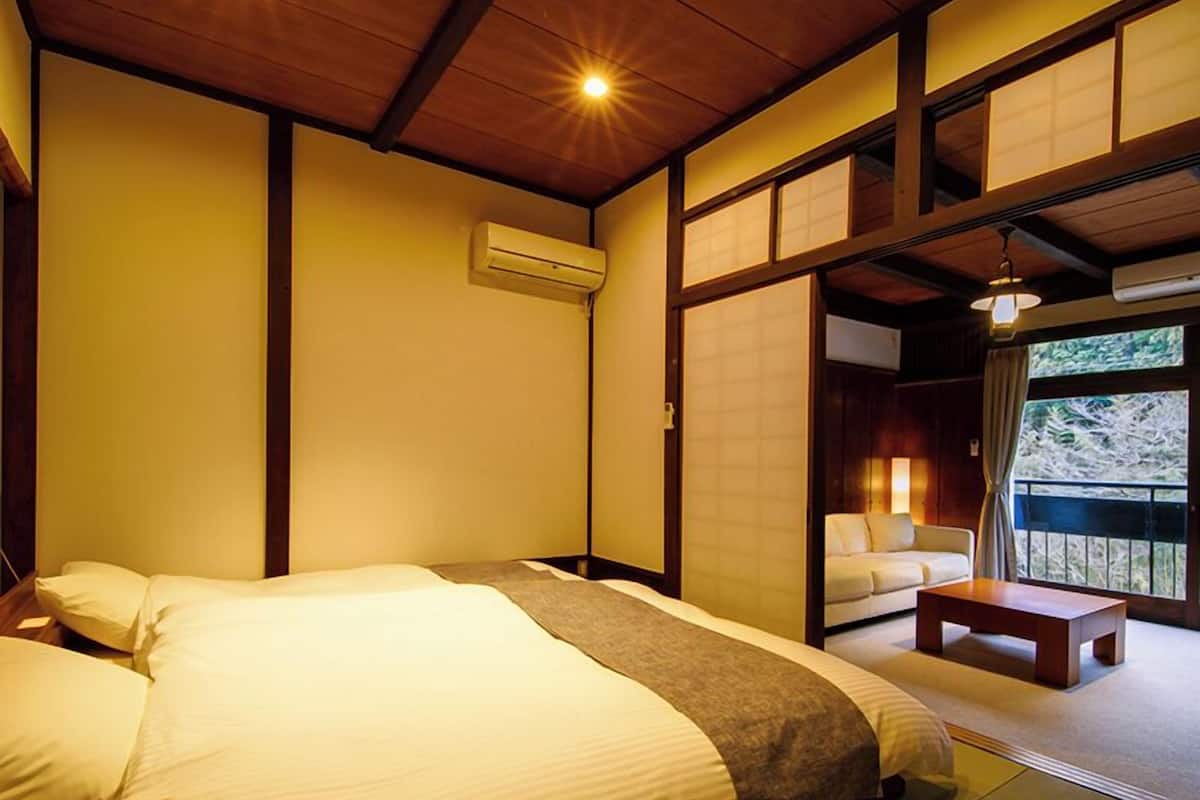 Ein traditionell gestaltetes japanisches Schlafzimmer mit einem großen Bett, einer Couch und Blick ins Freie.