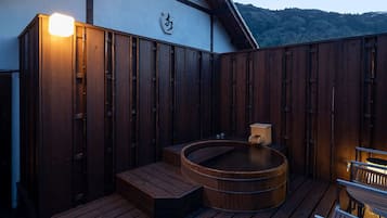 A wooden deck with a hot tub, wooden benches, and a white building with a wooden roof.