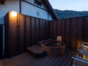 A wooden deck with a hot tub, wooden benches, and a white building with a wooden roof. - Shirakabeso (Izu)