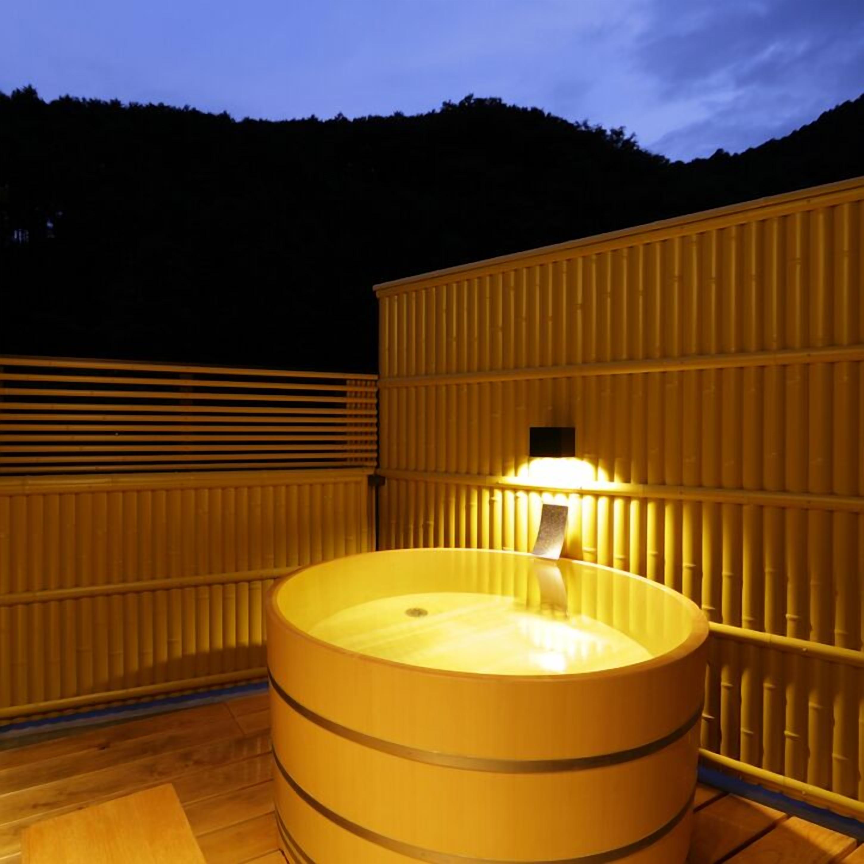 Een houten kuipvormige hottub met een lamp bovenop, omringd door houten panelen.