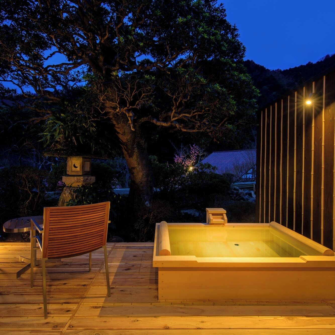 A wooden deck with a hot tub, a chair, and a tree in the background.
