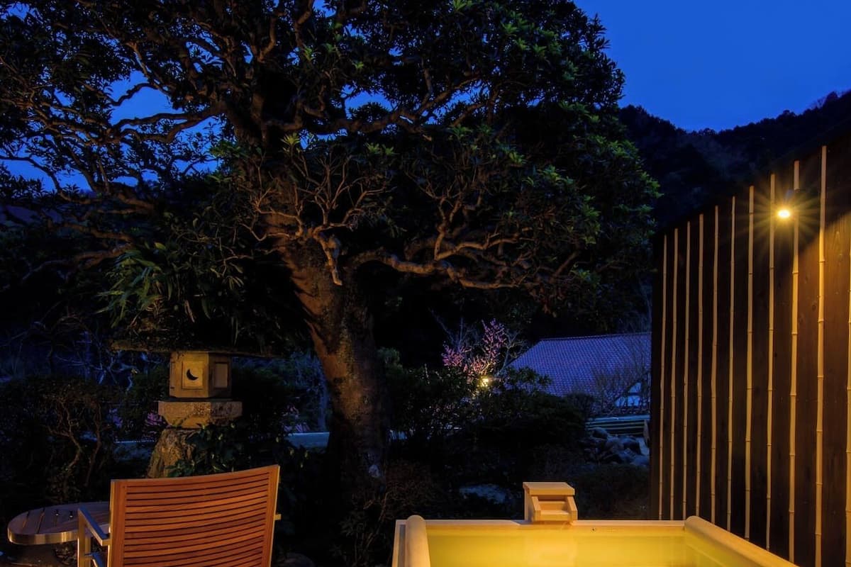 Eine Holzterrasse mit Whirlpool, einem Sessel und einem Baum im Hintergrund.