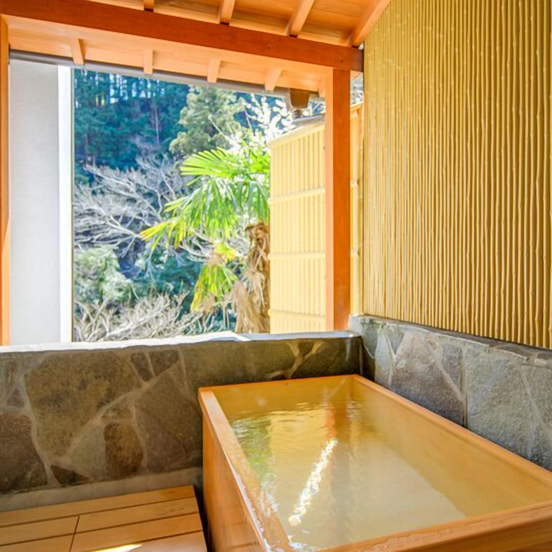 Een traditioneel Japans onsen met een houten kuip, stenen muren en uitzicht op groen.