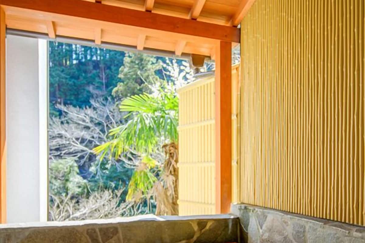 Ein traditionelles japanisches Onsen mit einer Holzwanne, Steinwänden und Blick auf grüne Vegetation.