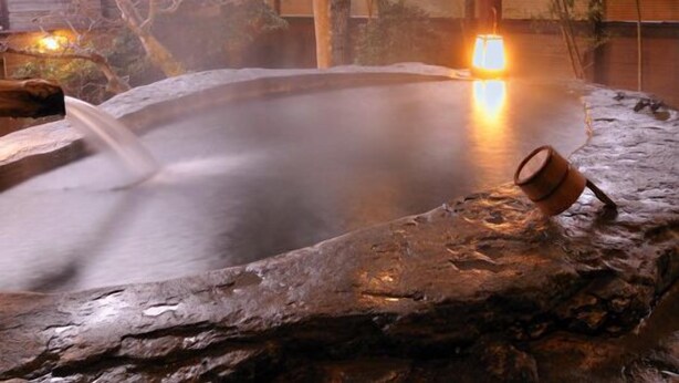 A hot spring bath area with a wooden structure overhead, stone seating, and a small wooden bucket. - Shirakabeso (Izu)
