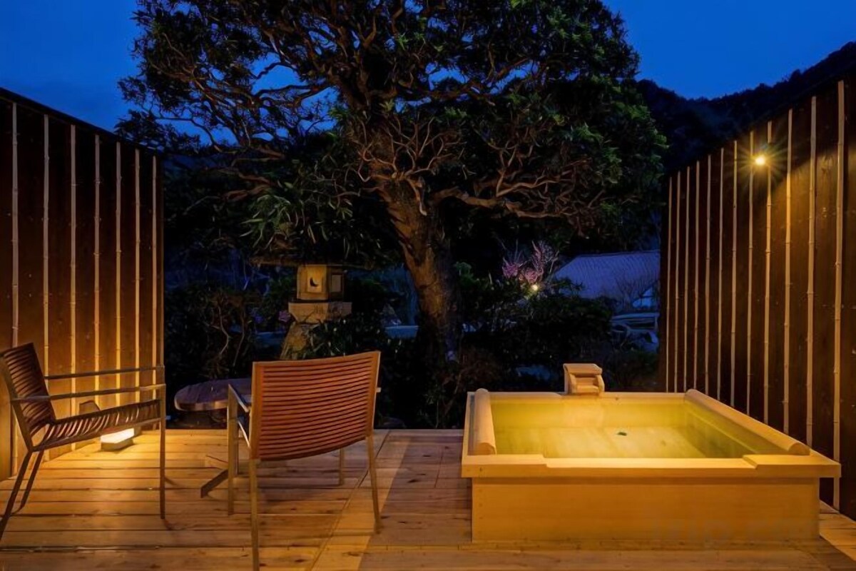 An outdoor patio with a hot tub, seating, and a tree.