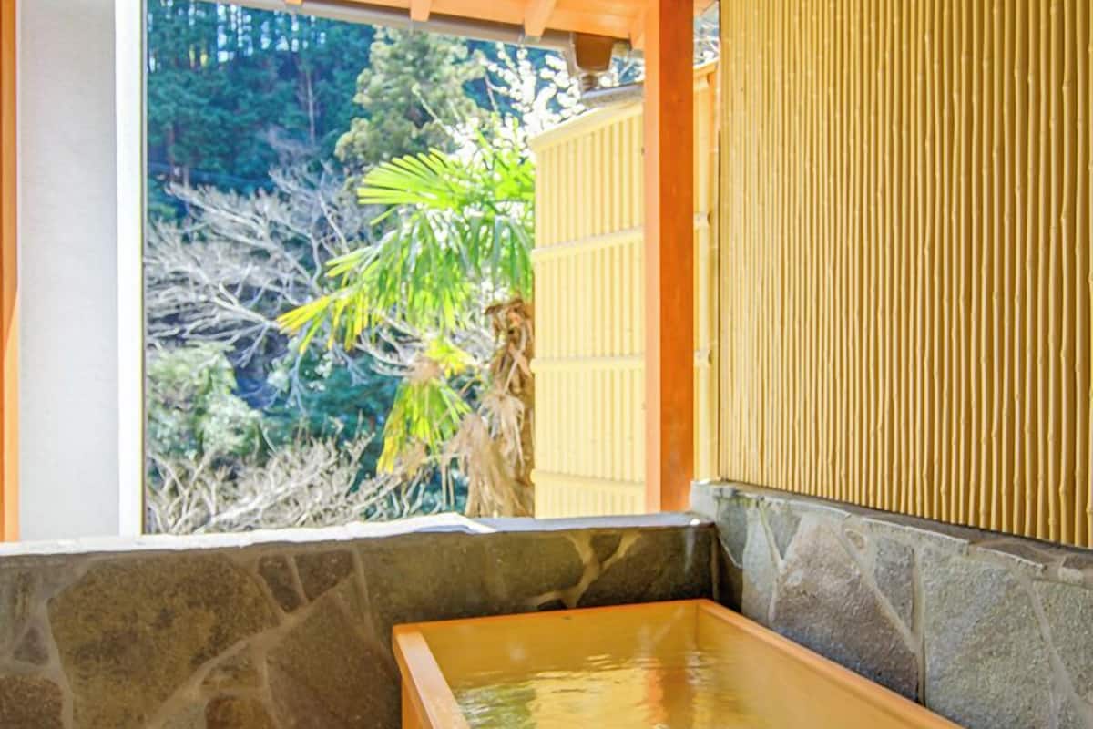 Ein traditionelles japanisches Onsen mit einem Steingrund-Bad, Holzliegen und Blick ins Grüne.