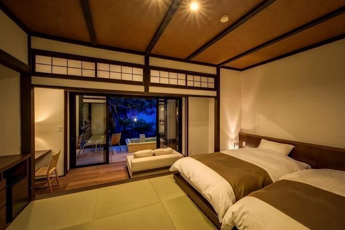 Ein traditionelles japanisches Schlafzimmer mit Tatami-Bodenbelag, einer Schiebetür, die zu einem Balkon führt, und einer niedrigen Holzbalkendecke.
