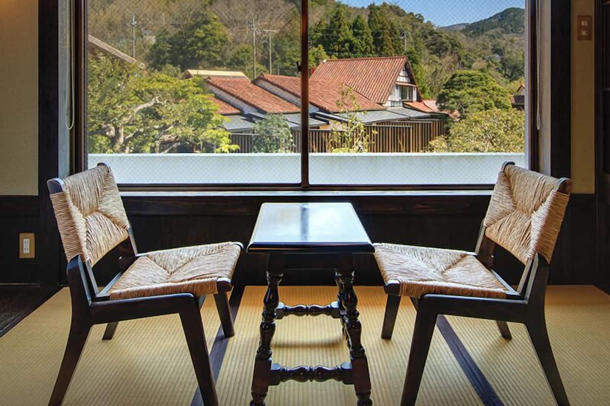 Ein Zimmer mit großem Fenster, zwei Stühlen, einem Tisch und einer traditionellen Lampe.
