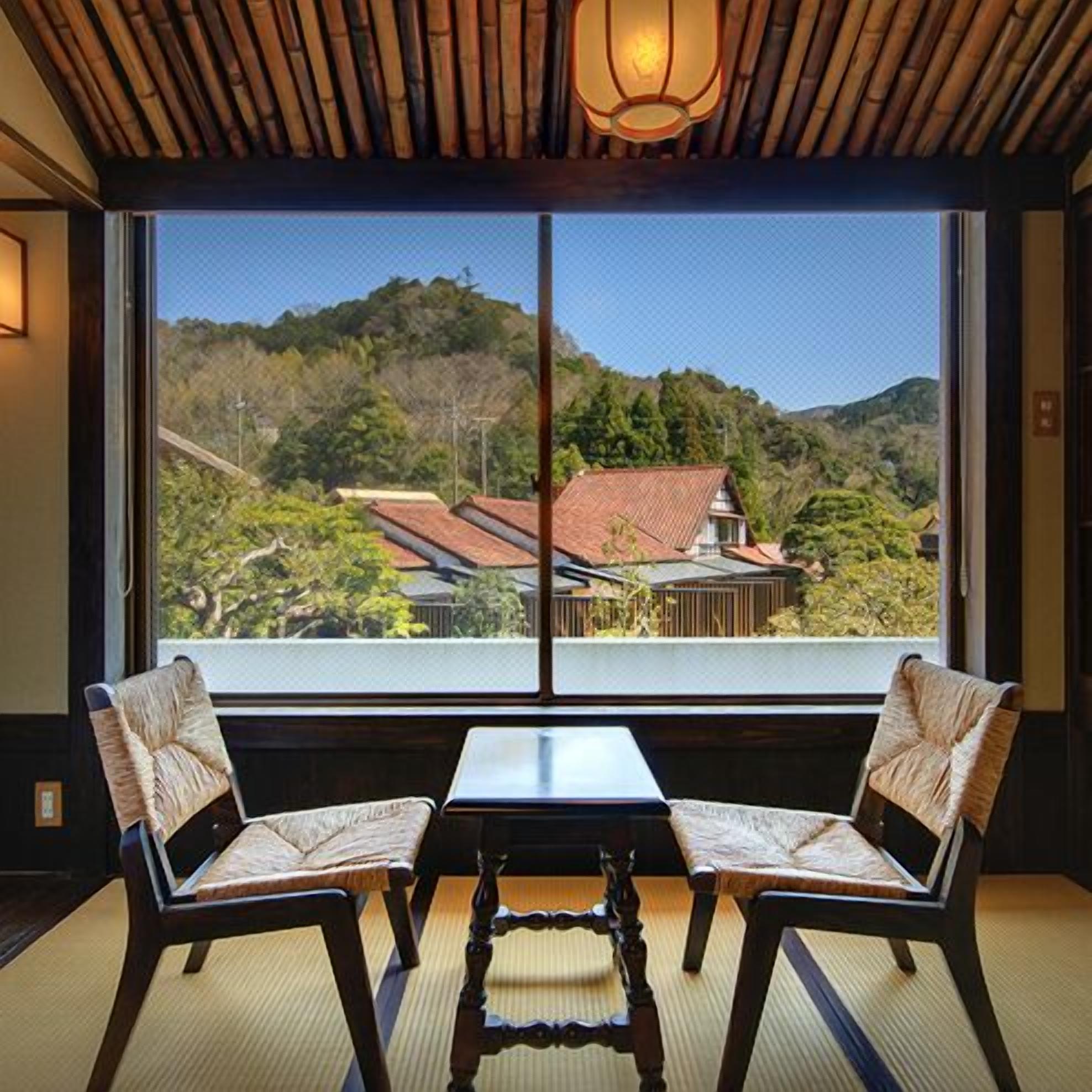 Een kamer met een groot raam, twee stoelen, een klein tafeltje en een traditionele Japanse lantaarn.