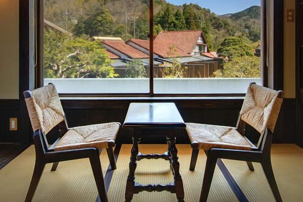Ein Zimmer mit großem Fenster, zwei Stühlen, einem kleinen Tisch und einer traditionellen japanischen Laterne.