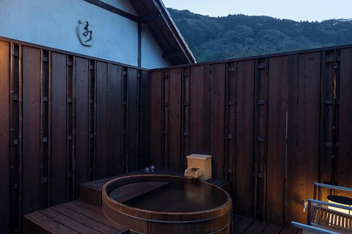 Eine Holzterrasse mit Whirlpool, einem kleinen Tisch und einer Bank.
