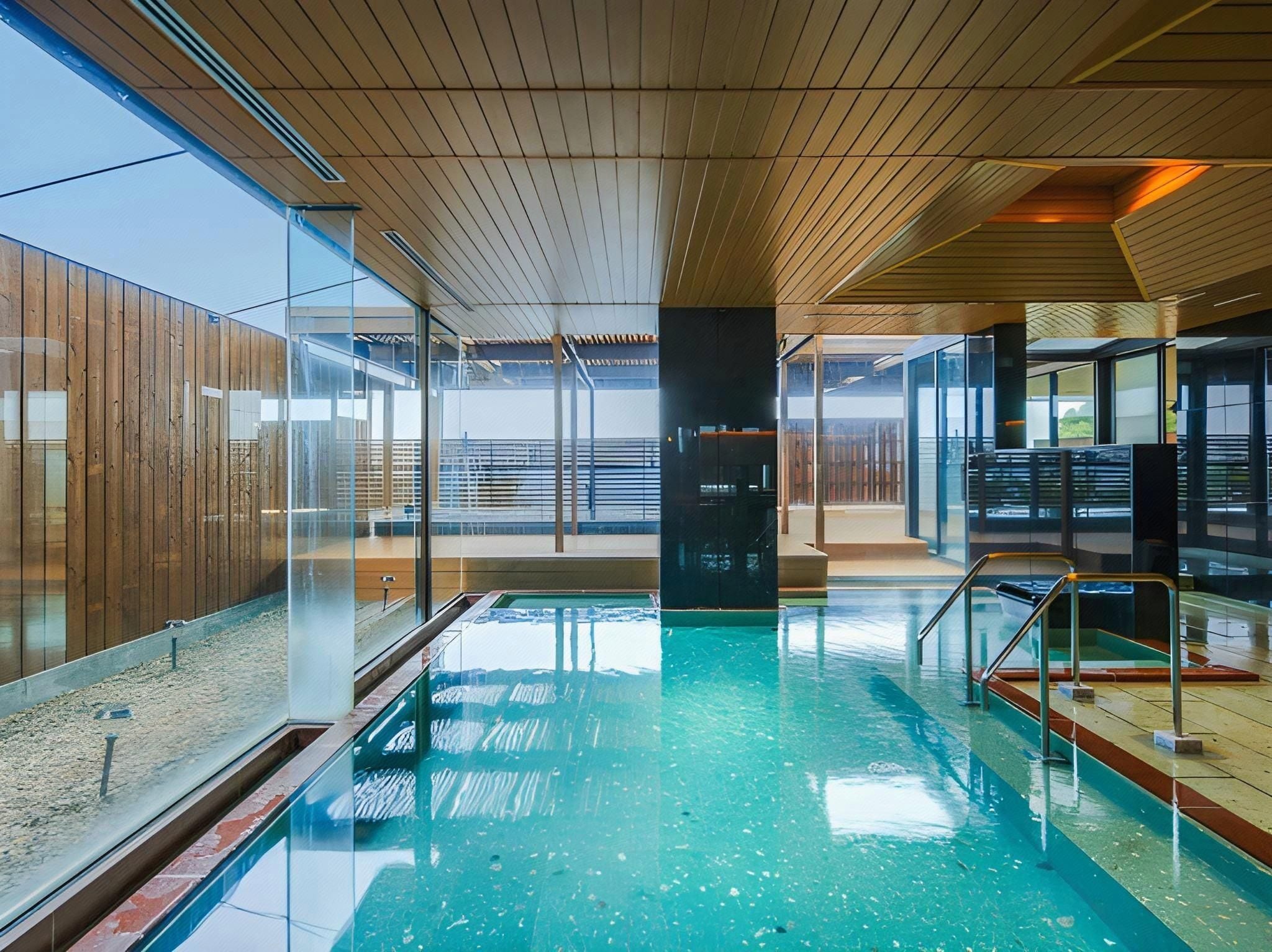 Una piscina interior amb parets de vidre, sostre de fusta i vista despejada cap a l'exterior.